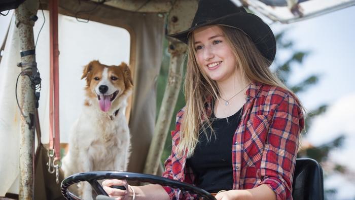 A dog sits next to a woman driving a tractor